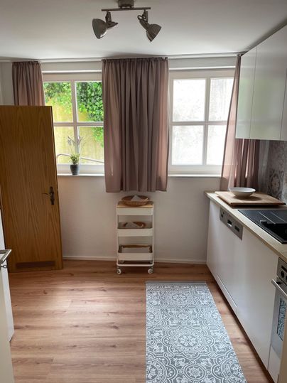 Großzügige Küche mit Holzfußboden und großen Fenstern. Im Abstellraum ist Platz für Ihr Reisegepäck.