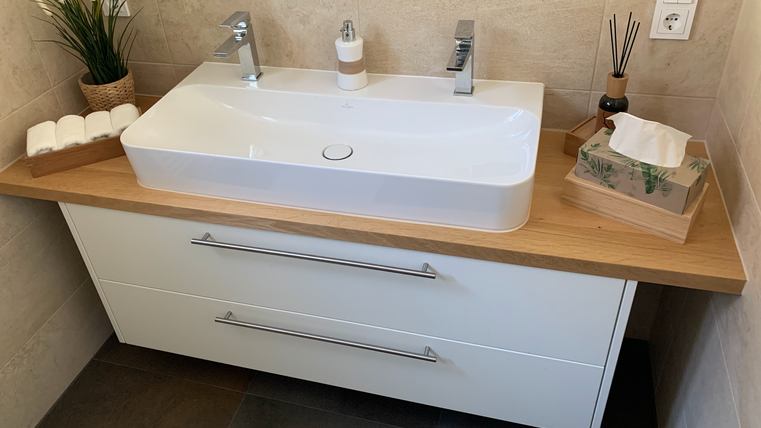 Ein modernes Badezimmer mit einem eleganten Waschbecken und Holzarbeitsplatte. Die Einrichtung ist hell und stilvoll, mit Pflanzen und Dekorationen.