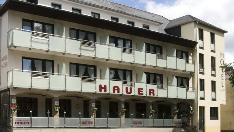 Ein modernes Hotel mit Balkonen und dem Namen „Hauer“ an der Fassade. Die Architektur ist elegant und einladend.