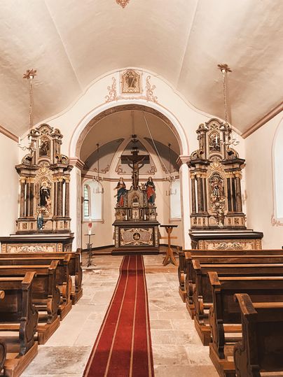 Eine ruhige Kirche mit Holzbenches und kunstvollen Altären. Der Boden ist mit einem roten Teppich bedeckt, der zur Mitte des Raumes führt.