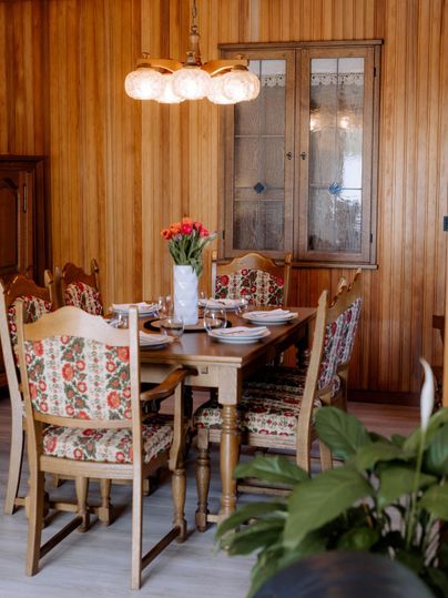 Een uitnodigende eetruimte met een houten tafel en kleurrijke stoelen. Op de tafel staat een vaas met bloemen en het servies is gedekt voor de maaltijd.