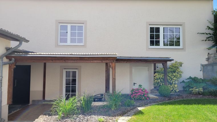 Ein modernes Haus mit einem gepflegten Garten und schönen Pflanzen. Der Eingang ist überdacht und die Fenster sind hell und einladend.