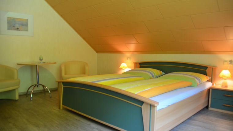 Ein gemütliches Schlafzimmer mit einem großen Doppelbett und zwei Stühlen. Das Zimmer hat eine warme Atmosphäre mit sanfter Beleuchtung.