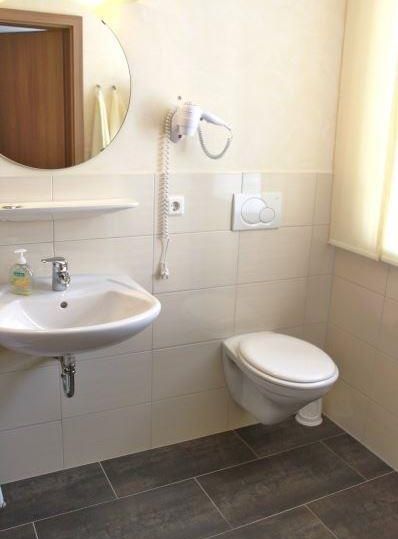 Une salle de bain simple avec un lavabo et des toilettes. Un miroir et un sèche-cheveux sont accrochés au mur.