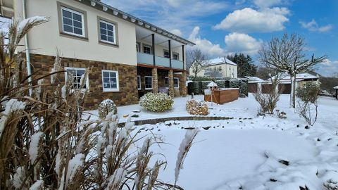 Une jolie maison avec un jardin recouvert de neige. Le ciel est dégagé et il y a quelques nuages.