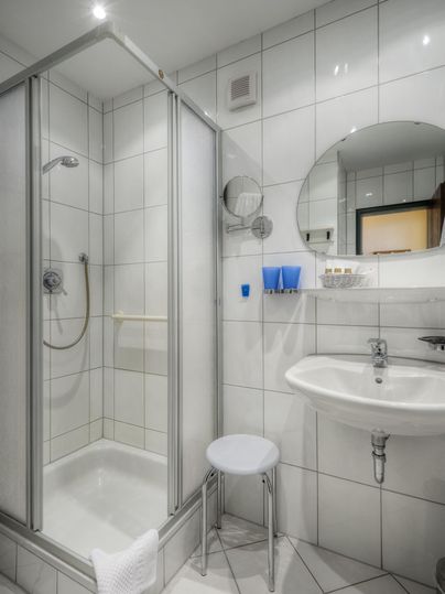 Ein modernes Badezimmer mit einer Duschkabine und einem Waschbecken. Weiße Fliesen und ein runder Spiegel vervollständigen das Design.