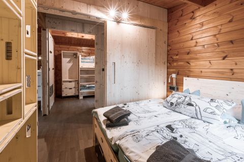 Une chambre moderne équipée d'un lit double et de lambris. La pièce est lumineuse et confortable, et s'ouvre directement sur un autre espace.