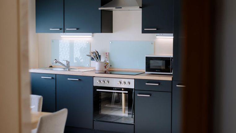 Een moderne keuken met donkerblauwe kasten en RVS apparaten. De ruimte is licht en uitnodigend, met een helder ontwerp.