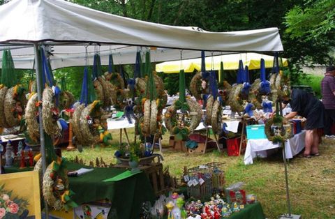 Ein Marktstand mit verschiedenen dekorativen Kränzen hängt an einem weißen Zelt. Im Hintergrund sind weitere Stände und Besucher zu sehen.