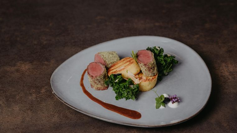 Ein elegantes Gericht mit zartem Fleisch, umgeben von Gemüse und einer dekorativen Sauce. Das Essen ist ansprechend auf einem modernen Teller arrangiert.