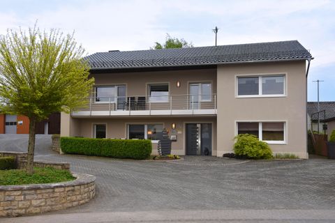 Ein modernes Haus mit einem Balkongeländer und einem gepflegten Vorgarten. Die Fassade ist in sanften Farben gehalten und das Grundstück ist gut angelegt.
