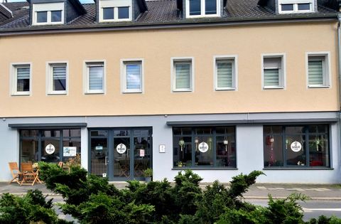 Ein modernes Geschäftshaus mit einer hellen Fassade. Vor dem Gebäude stehen einige Möbel und es gibt große Fenster mit einladenden Schildern.