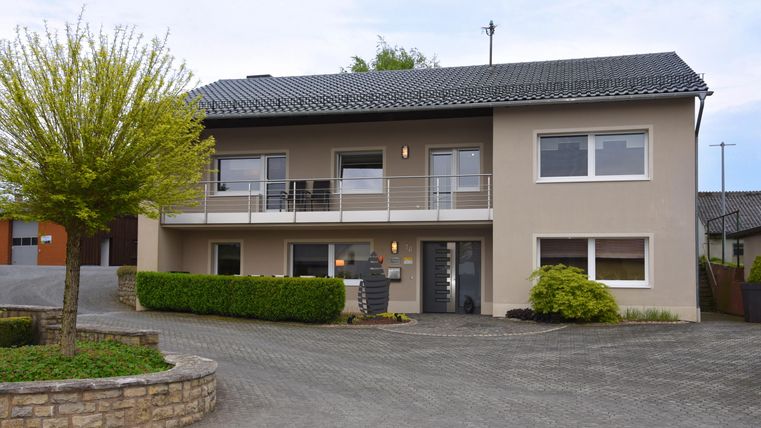 Ein modernes Haus mit einem Balkongeländer und einem gepflegten Vorgarten. Die Fassade ist in sanften Farben gehalten und das Grundstück ist gut angelegt.