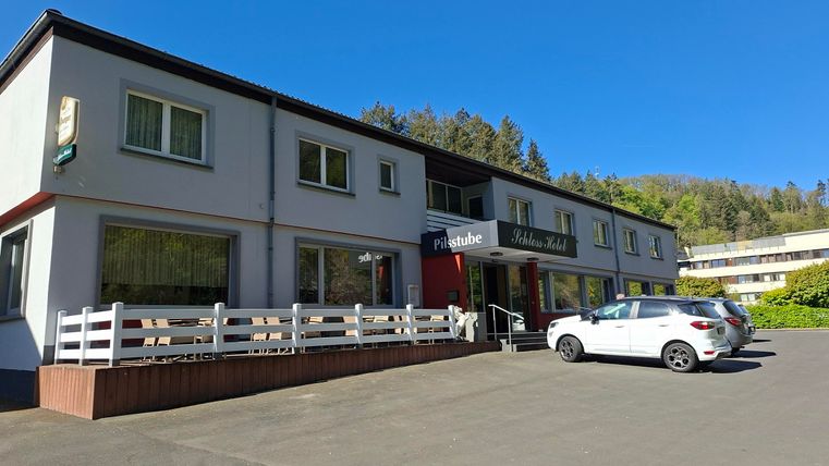 Une petite auberge avec une façade claire et une entrée accueillante. Devant le bâtiment, plusieurs voitures sont garées.