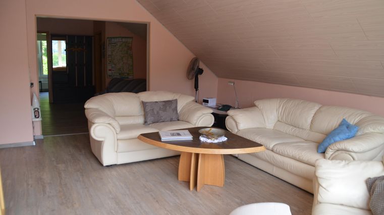 Gemütliches Wohnzimmer mit weißen Ledersofas und einem runden Tisch. Die Wände sind in einem sanften Rosaton und der Raum hat eine helle, einladende Atmosphäre.