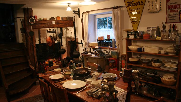 Eine rustikale Küche mit einem Tisch, der für eine Mahlzeit gedeckt ist. An den Wänden hängen verschiedene alte Utensilien und Schilder.