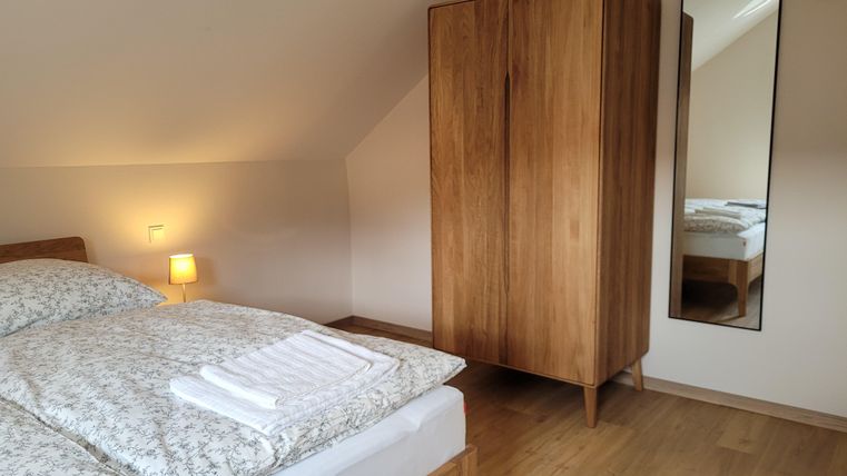 Ein gemütliches Schlafzimmer mit einem großen Bett und einem Holzschrank. Eine Lampe und ein Spiegel vervollständigen die moderne Einrichtung.
