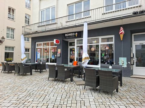 Een café met buitenterrassen en zonnenschermen. Het gebouw heeft grote ramen en een uitnodigende sfeer.