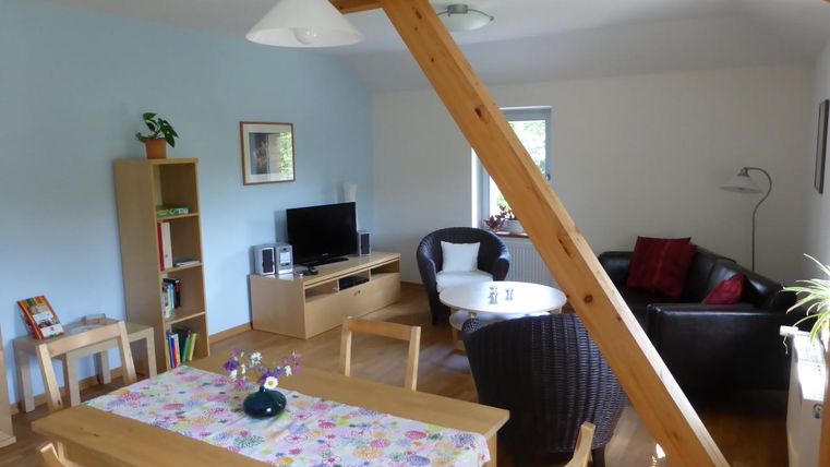 Ein helles Wohnzimmer mit Holzmöbeln und einem großen Esstisch. Die gemütliche Sitzecke lädt zum Entspannen ein.