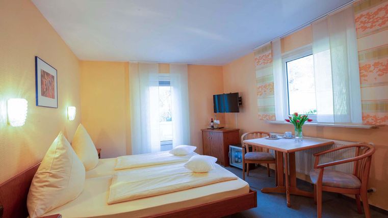 Ein gemütliches Zimmer mit zwei Betten und einem Tisch. Das Zimmer hat helle Wände und ein Fenster, das viel Licht hereinlässt.