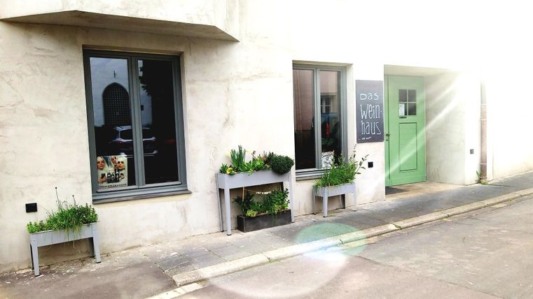 Ein modernes Gebäude mit zwei Fenstern und einer grünen Tür. Vor dem Haus stehen Blumenkästen mit Pflanzen.