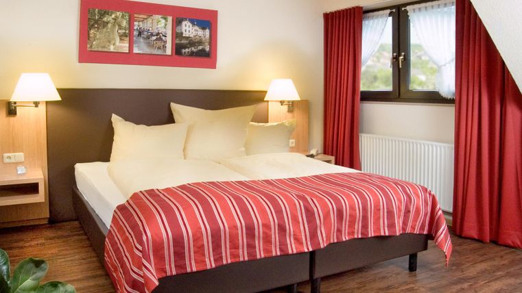 Ein gemütliches Schlafzimmer mit einem großen Bett und roten Vorhängen. Sanfte Beleuchtung schafft eine einladende Atmosphäre.