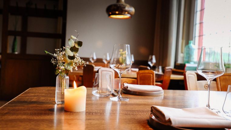 Ein wunderschöner Tisch in einem Restaurant, dekoriert mit einer kleinen Blumenvase und einer Kerze. Der Raum hat eine gemütliche Atmosphäre mit sanftem Licht.