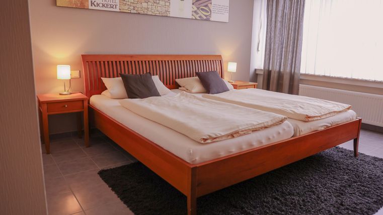 Ein gemütliches Schlafzimmer mit einem großen Doppelbett und zwei Nachttischen. Das Zimmer ist hell und freundlich, mit einem modernen Teppich und Vorhängen.