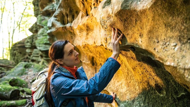 Eine Frau berührt eine Sandsteinwand im Wald.