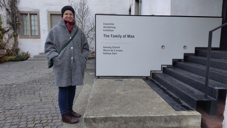 Een persoon staat voor een gebouw met een bord dat "The Family of Man" toont. De plek lijkt modern en uitnodigend.