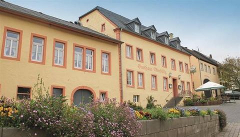 Ein elegantes gelbes Gebäude mit mehreren Fenstern und einem Vordach. Es gibt Blumenbeete und einen kleinen Platz im Vordergrund.