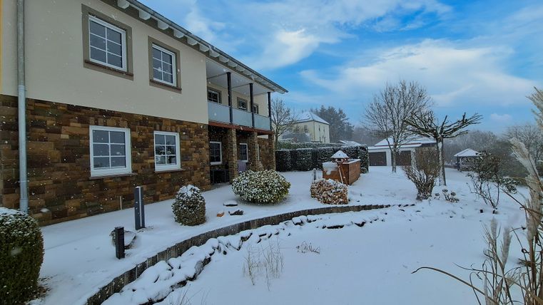 Ein Haus im Schnee mit einem gepflegten Garten. Der Himmel ist blau mit einigen Wolken.