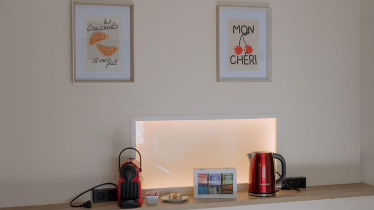 Een gezellige hoek met een waterkoker, een koffiemachine en een kleine selectie thee. Aan de muur hangen twee schilderijen met Franse opschriften.