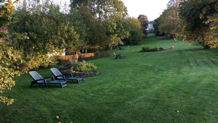 Ein gepflegter Garten mit grünem Rasen und Bäumen. Im Vordergrund stehen zwei Liegestühle zum Entspannen.