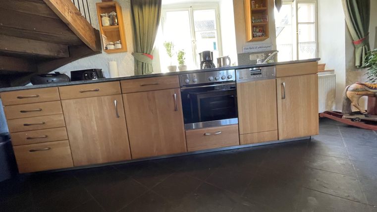 Eine moderne Küche mit Holzschränken und einer Kochplatte. Große Fenster sorgen für viel Tageslicht.