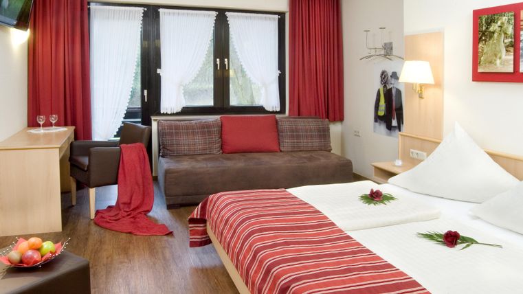 Ein modernes Zimmer mit einem Doppelbett und einem gemütlichen Sofa. Die Wände sind in warmen Farbtönen gehalten, und ein Tisch mit frischen Früchten steht bereit.