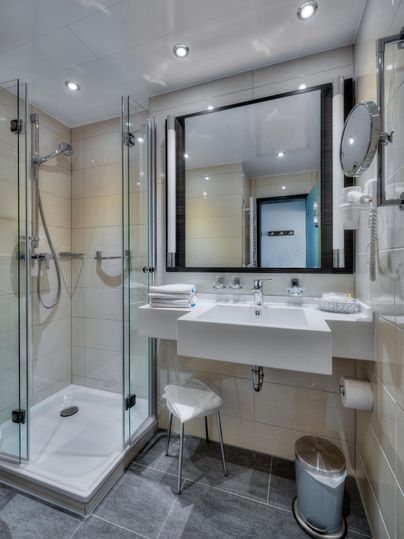 Ein modernes Badezimmer mit einer Glasdusche und einem schlichten Waschbecken. Der Raum ist hell und gut beleuchtet.