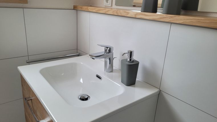 Ein modernes Badezimmer mit einem weißen Waschbecken und einem eleganten Wasserhahn. Auf dem Regal stehen dekorative graue Behälter.