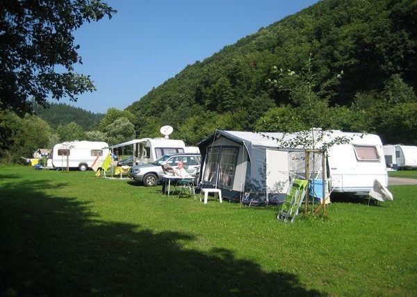 Eine malerische Campingplatz mit Wohnmobiles und Wohnwagen auf grüner Wiese. Im Hintergrund sind sanfte Hügel und Bäume zu sehen.