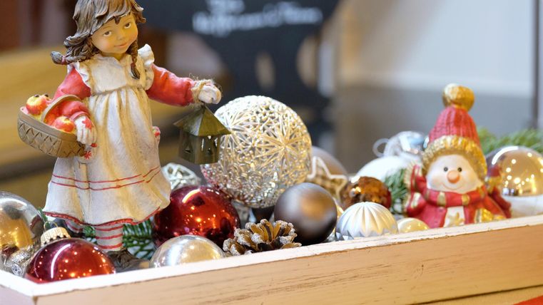 Eine festliche Dekoration mit einer kleinen Figur eines Mädchens, das eine Laterne trägt. Um sie herum befinden sich bunte Weihnachtskugeln und eine Schneemannfigur.