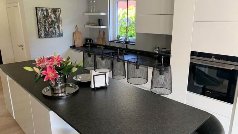 Moderne Küche mit einem eleganten Küchentresen und stilvollen Lampen. Frische Blumen verleihen dem Raum eine einladende Atmosphäre.