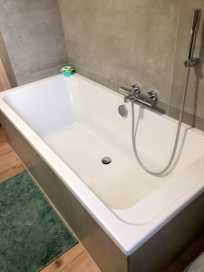 Eine moderne Badewanne mit einem minimalistischen Design. Der Boden ist aus Holz und ein grüner Teppich liegt davor.