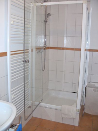 Ein modernes Badezimmer mit einer Duschkabine und weißen Fliesen. Neben der Dusche steht ein Waschbecken.