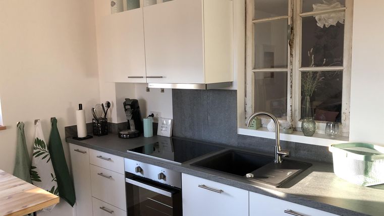 Een moderne keuken met witte kasten en een zwart aanrecht. Op de achtergrond zijn een raam en enkele decoratieve voorwerpen te zien.