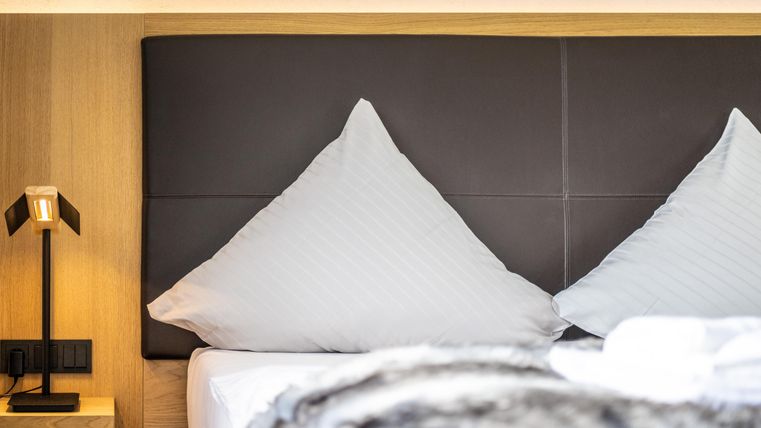 Ein modernes Schlafzimmer mit einem großen Bett und stilvollen Kissen. Neben dem Bett steht eine elegante Nachttischlampe.