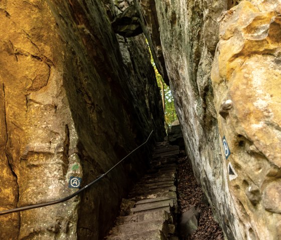 A narrow path with stone steps leads through a narrow rocky gorge. The walls are steep and illuminated by natural light., &copy; Dominik Ketz