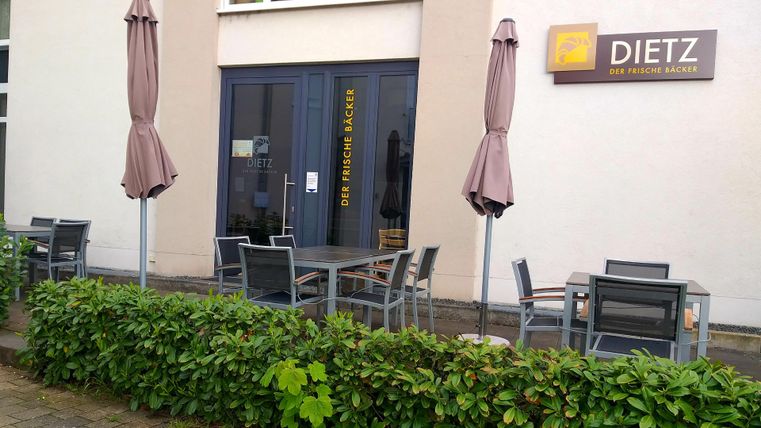 Ein Außenbereich eines Restaurants mit Tischen und Stühlen. Einige Sonnenschirme stehen auf der Terrasse.