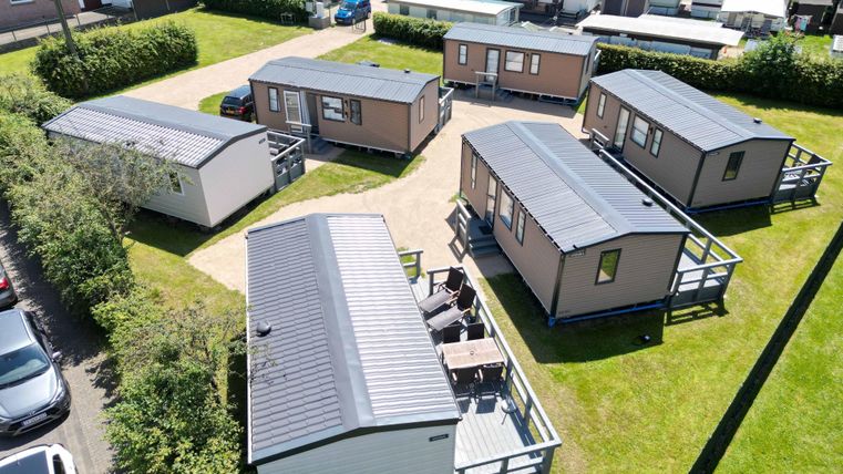 Eine Gruppe von Ferienhäusern auf einem grünen Grundstück. Die Häuser sind modern und gut angeordnet, umgeben von Bäumen und Grasflächen.