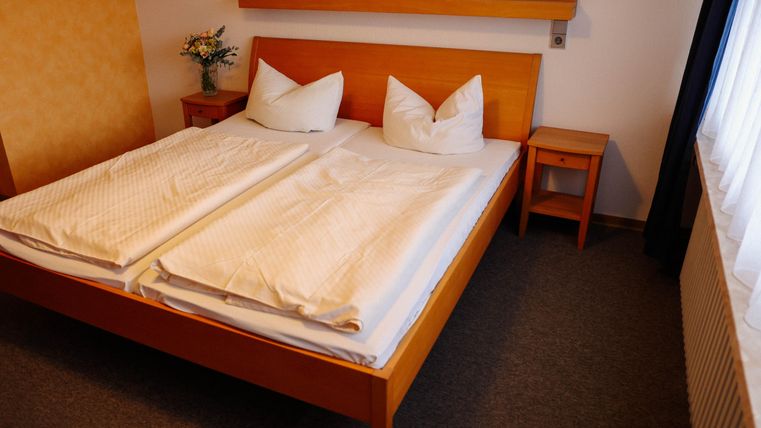 Ein gemütliches Schlafzimmer mit einem Doppelbett und zwei Kissen. Neben dem Bett steht ein Nachttisch und es gibt einen Blumenstrauß auf der Fensterbank.