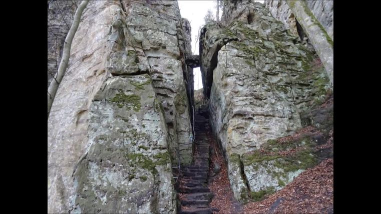 Eine schmale Passage zwischen hohen, moosbedeckten Felsen. Eine Treppe führt durch den Spalt nach oben.